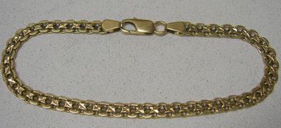 gros plan d'un bracelet en chaîne en or sur une surface blanche