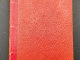 an old book with a red cover sitting on top of a table