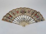 an old fan with a floral design on it sitting on a white surface