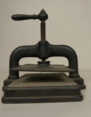an old iron press is sitting on top of a white surface