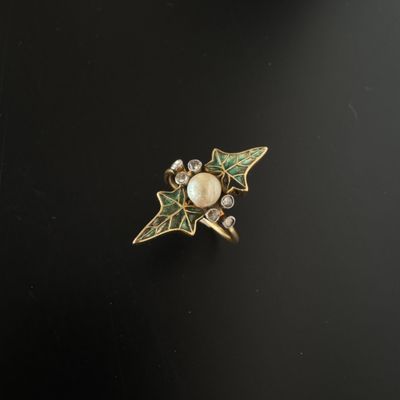 un gros plan d'une bague en or ornée d'une perle et de feuilles vertes