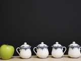 four cups and an apple sit on a table in front of a black background