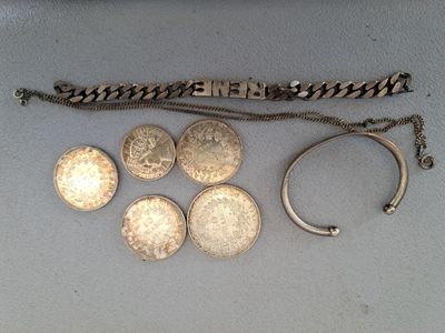Plusieurs pièces d'argent et un bracelet sont posés sur une surface blanche