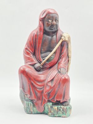 statue d'un homme assis sur un rocher, tenant un bâton