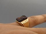 a man ' s hand holding a gold ring with a cupcake on it