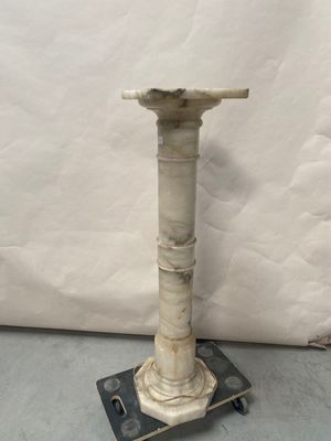 une image représentant un piédestal blanc avec une base métallique posé sur un sol gris