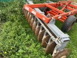 a close up of a tractor plow in the grass near a building