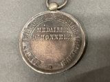 silver medal with the name of a person on it on a gray surface