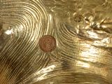 a close up of a gold vase with a coin on it
