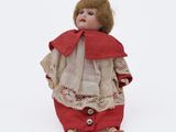 an old doll with a red cape and red pants sitting on a white surface