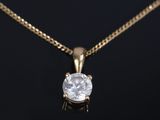 a diamond pendant on a gold chain on a black background