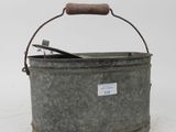 a metal bucket with a wooden handle on a white surface