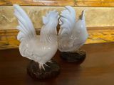 pair of white glass rooster figurines sitting on top of a wooden table