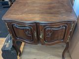 une petite table en bois à deux tiroirs, avec une valise posée à côté