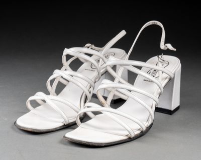 une paire de sandales en cuir blanc à lanières, posées sur un fond gris