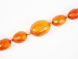 un gros plan sur un collier de perles de verre orange posé sur une surface blanche
