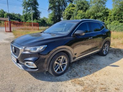 un SUV Volvo noir garé sur un chemin de gravier devant des arbres