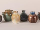 seven vases sitting in a row on a white surface