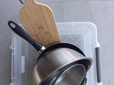 des casseroles et des poêles rangées dans un bac en plastique avec une spatule en bois