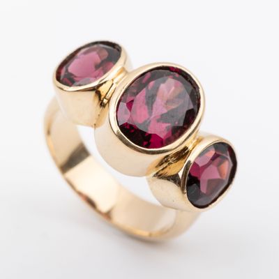 a close up of a gold ring with three oval garnets