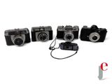 four old cameras are lined up in a row on a white surface