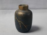 a small black vase with a gold design on it