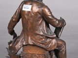 bronze statue of a man sitting on a chair with a book in his lap