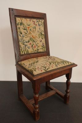 une vieille chaise en bois dont l'assise est recouverte d'un tissu à motifs floraux, posée sur une surface noire