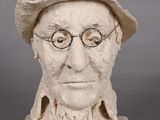 statue d'un homme portant des lunettes et un chapeau, posée sur une surface grise