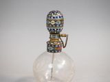 une petite bouteille en verre munie d'une poignée en métal, posée sur une surface blanche