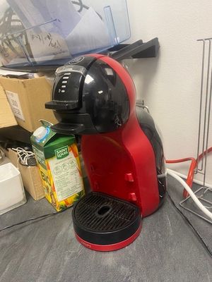 une cafetière rouge posée sur un plan de travail, à côté d'une grille métallique