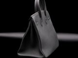 black leather handbag sitting on a black surface with a black background