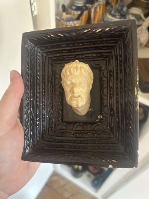 a person holding a picture of a gold head in a black frame