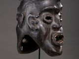 a close up of a wooden mask on a stand on a gray background