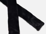 L'écharpe en fourrure noire est posée sur une surface blanche.
