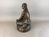 bronze statue of a woman sitting on a rock with her legs crossed