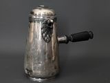 une cafetière ancienne en argent, avec une poignée noire sur fond gris