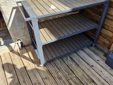 une table en bois posée sur une terrasse en bois, près d'un mur en pierre