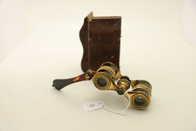 une paire de jumelles anciennes posées sur une surface blanche, accompagnées d'un étui marron