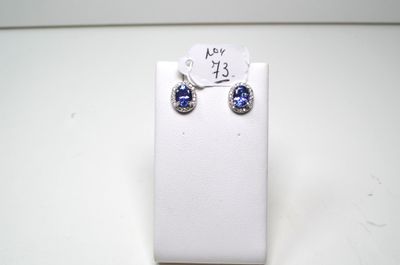 une paire de boucles d'oreilles en saphir bleu et diamants, présentée sur un présentoir blanc