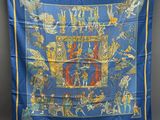 un foulard en soie bleu et jaune orné de motifs représentant des personnes et des animaux