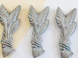 three silver leaves on a white surface next to a piece of paper
