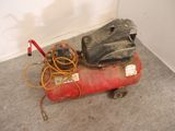 a red air compressor sitting on the floor next to a wall