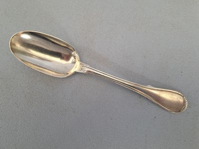 une cuillère en argent posée sur une surface grise, avec une autre cuillère en argent au milieu