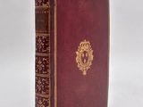 an old red book with gold trim sitting on top of a white surface