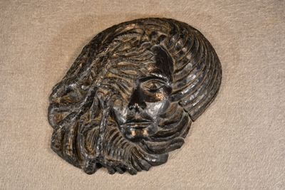 une sculpture métallique représentant le visage d'un homme sur une surface beige