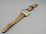 une image représentant une montre avec un bracelet en cuir posée sur une surface grise