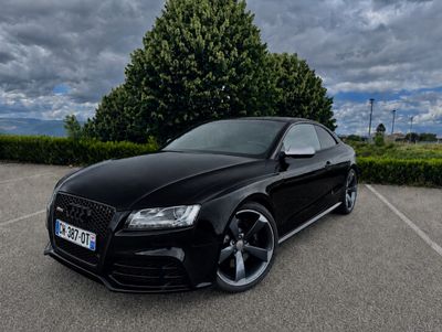 La voiture noire est garée sur un parking sous un ciel nuageux.