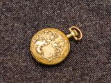 une image représentant une montre de poche en or posée sur un tissu marron