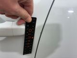 a hand that is holding a ruler in front of a white car